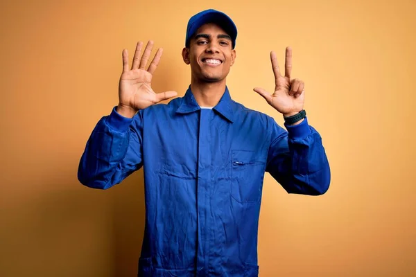 年轻的非洲技师 身穿蓝色制服 头戴黄色背景帽 头戴八号手指 面带微笑 自信而快乐 — 图库照片