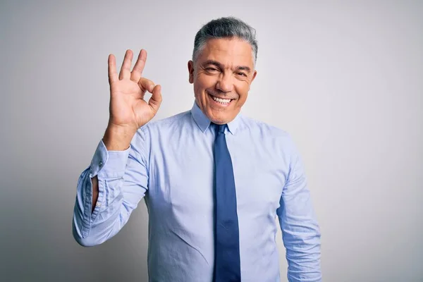 Middle age handsome grey-haired business man wearing elegant shirt and tie smiling positive doing ok sign with hand and fingers. Successful expression.