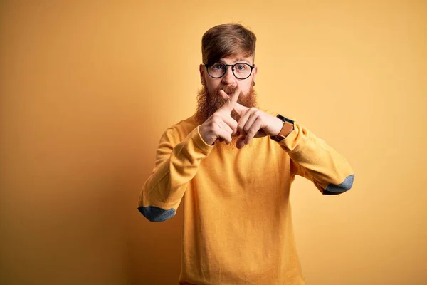 Handsome Irish redhead man with beard wearing glasses over yellow isolated background Rejection expression crossing fingers doing negative sign