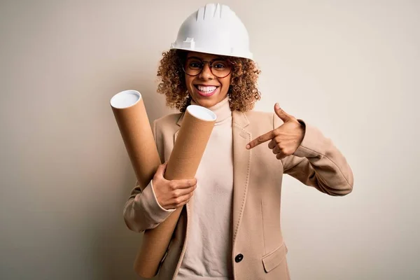 非洲裔美国妇女 卷曲的建筑师 戴着安全帽 戴着眼镜 手里拿着设计图 满脸惊讶地指着自己 — 图库照片