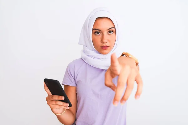 若いです美しいですアラビア語の女の子を身に着けていますヒジャーブスマートフォンを使用して隔離された白い背景の上に指でカメラを指して あなたに 手のサイン 正とフロントから自信を持ってジェスチャー — ストック写真