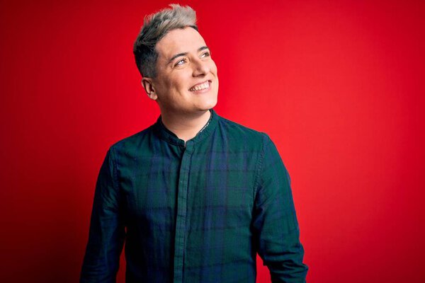 Young handsome modern man wearing elegant green shirt over red isolated background looking away to side with smile on face, natural expression. Laughing confident.