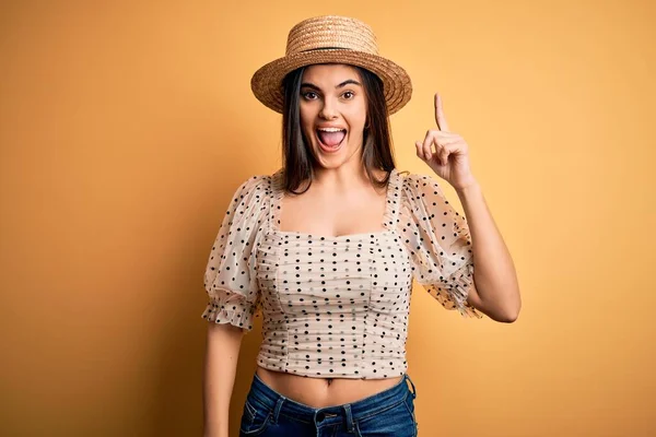 若い美しいブルネットの女性は 成功したアイデアで指を指す黄色の背景にTシャツと夏の帽子を身に着けています 興奮し 第一番 — ストック写真
