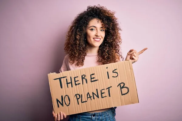 Young beautiful activist woman with curly hair and piercing protesting asking for change planet very happy pointing with hand and finger to the side