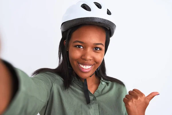 年轻的非洲裔美国女人戴着自行车头盔 带着自拍的样子 带着孤独的背景 手指朝外 笑容满面的站在一旁 — 图库照片