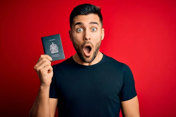 Junger Gutaussehender Touristenmann Mit Kanadischem Reisepass Über Rotem Hintergrund Erschrocken — Stockfoto