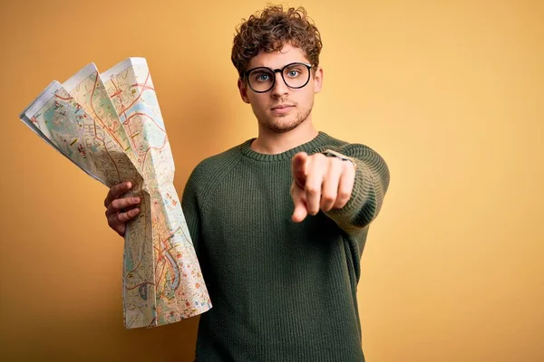 若いですブロンド観光客男オン休暇とともに巻き毛保持市地図上の黄色の背景ポインティング上の指でカメラとあなたに 手のサイン 正と自信のジェスチャーからフロント — ストック写真