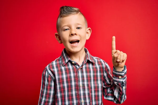 青い目の若い白人の子供は 赤い背景の上にエレガントなシャツを着て立って 成功したアイデアで指を指しています 興奮し 第一番 — ストック写真