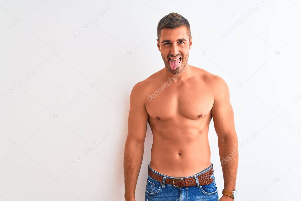 Young handsome shirtless man showing muscular body over isolated background sticking tongue out happy with funny expression. Emotion concept.