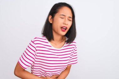 Young chinese woman wearing striped t-shirt standing over isolated white background with hand on stomach because indigestion, painful illness feeling unwell. Ache concept.
