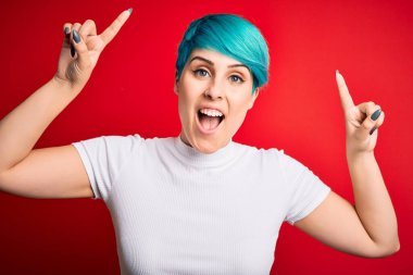 Mavi saçlı, kırmızı arka planda rahat tişörtler giyen genç ve güzel bir kadın. Şaşırmış, şaşırmış, parmaklarıyla işaret ediyor ve kollarını kaldırıyordu..