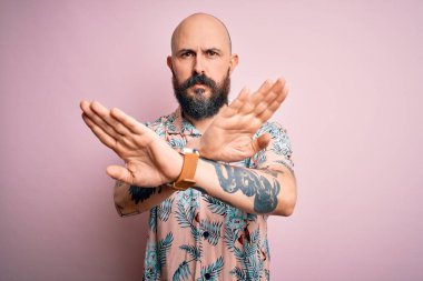 Sakallı ve dövmeli yakışıklı bir adam pembe arka planda sıradan bir çiçek gömleği giyiyor.