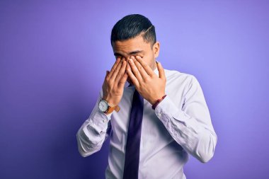 İzole edilmiş mor arka plan üzerinde duran zarif kravat takan genç Brezilyalı işadamı yorgunluk ve baş ağrısı için gözlerini ovuşturuyor, uykulu ve yorgun ifade ediyor. Görüş sorunu