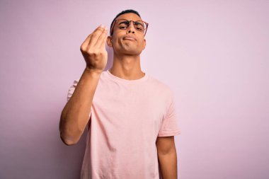 Yakışıklı Afro-Amerikalı adam pembe arka planda günlük tişört ve gözlük takıyor. İtalyan jestleri yapıyor.