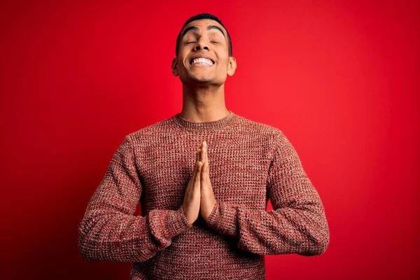 Young handsome african american man wearing casual sweater standing over red background begging and praying with hands together with hope expression on face very emotional and worried. Begging.