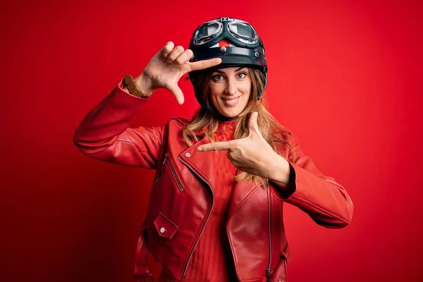 赤い背景に元ヘルメットを身に着けている若い美しいブルネットのオートバイの女性は幸せな顔を持つ手と指でフレームを作り笑顔 創造性と写真の概念 — ストック写真