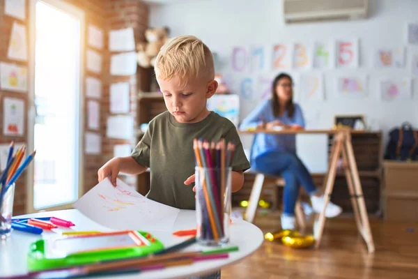 若い白人の子供は教師と一緒に学校で遊んでいる 母と息子は遊び場で色鉛筆で絵を描く若い女性は机の上に座っている — ストック写真