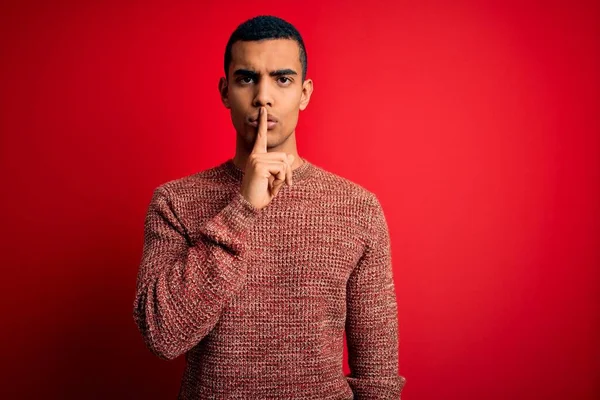 年轻英俊的非洲裔美国男人穿着宽松的毛衣站在红色的背景上 要求保持安静 手指放在嘴唇上 沉默和秘密概念 — 图库照片
