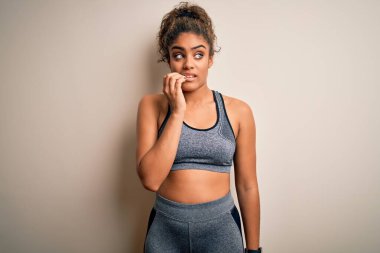 Genç Afro-Amerikan sporcu kadın spor yapıyor beyaz arka plan üzerine spor giysisi giyiyor gergin ve elleri ağızdan tırnak yerken gergin görünüyor. Endişe sorunu.