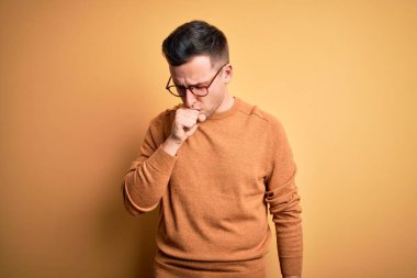 Sarı arka plan üzerinde gözlük takan yakışıklı beyaz bir adam kendini iyi hissetmiyor ve bronşitin belirtileri olarak öksürüyor. Sağlık hizmeti kavramı.