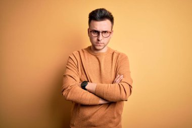 Sarı arka plan üzerinde gözlük takan yakışıklı, beyaz bir adam kuşkucu ve gergin kolları çaprazlanmış bir yüz ifadesini tasvip etmiyor. Negatif kişi.