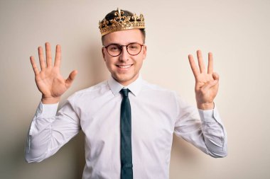 Soyutlanmış arka planda altın taç takan yakışıklı beyaz iş adamı sekiz numaralı parmaklarını gösterip gülümserken kendinden emin ve mutlu görünüyor..