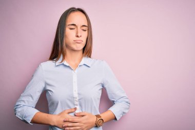 Zarif bir gömlek giyen genç ve güzel bir iş kadını midesi üzerinde pembe bir arka planda duruyor çünkü hazımsızlık, acı verici bir hastalık, kendini iyi hissetmiyor. Ache kavramı.