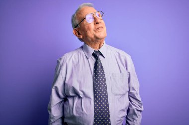 Gri saçlı, gözlüklü, mor izole edilmiş arka planda duran kıdemli iş adamı. Gülümsüyor ve uzaklara bakıyor..