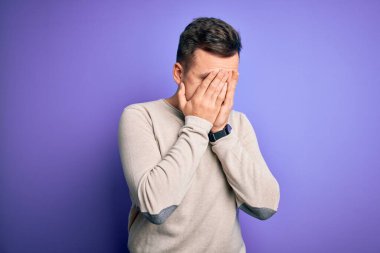 Mor izole arka plan üzerine günlük süveter giyen yakışıklı beyaz bir adam ve ağlarken suratını ellerle kapatan üzgün bir yüz ifadesi. Depresyon kavramı.