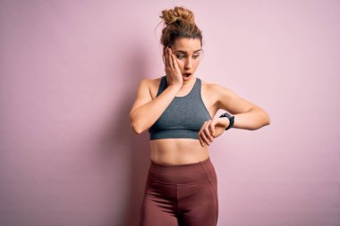 Genç, güzel, sarışın, spor yapan, spor giyinen, pembe arka planda spor giyinen bir kadın.