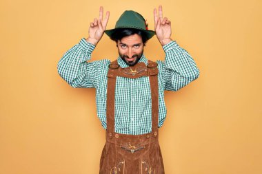Almanya festivali için geleneksel Alman Ekim Festivali kıyafeti giyen genç yakışıklı adam komik ve çılgın pozlar veriyor parmakları kafasında tavşan kulağı, neşeli bir gülümseme