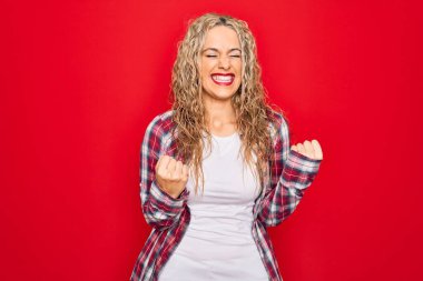 Genç ve güzel sarışın bir kadın yalnız kırmızı arka planda dikilmiş kolları havada ve gözleri kapalı bir şekilde başarıyı kutluyor ve şaşırıyor. Kazanan konsept.