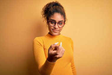 Sarı arka planda süveter ve gözlük takan güzel Afro-Amerikan kızı seni buraya davet ediyor.