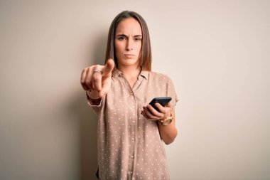 Genç ve güzel bir kadın akıllı telefon kullanarak kamerayı işaret eden cep telefonuna bakıyor ve sen, el işareti, ön taraftan pozitif ve kendinden emin bir hareket.