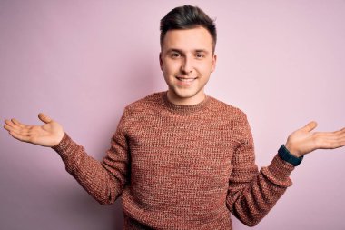 Pembe izole edilmiş arka planda sıradan bir kazak giyen yakışıklı beyaz bir adam gülümseyerek avuçlarını açıyor, sunuyor ve reklam karşılaştırması yapıyor ve dengeyi sağlıyor.