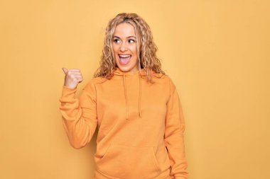 Sarışın, güzel ve sportif bir kadın sarı arka planda rahat bir eşofman giyiyordu. Gülümsüyor, gülümsüyor ve başparmağıyla yan tarafa bakıyordu..