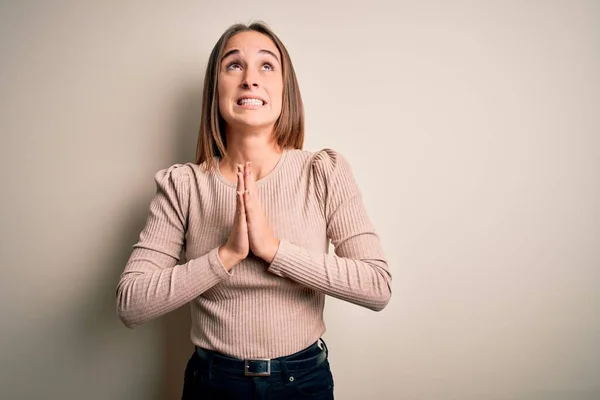 Young beautiful woman wearing casual sweater standing over isolated white background begging and praying with hands together with hope expression on face very emotional and worried. Begging.