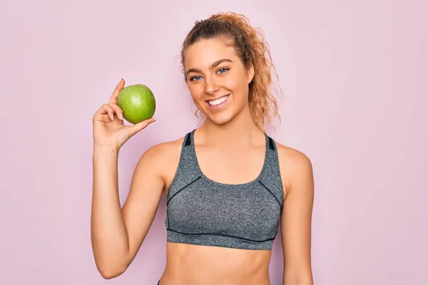 年轻美丽的金发女运动员 蓝眼睛 长着健康的绿色苹果果实 脸上挂着快乐的表情 脸上挂着自信的微笑 露出牙齿 — 图库照片