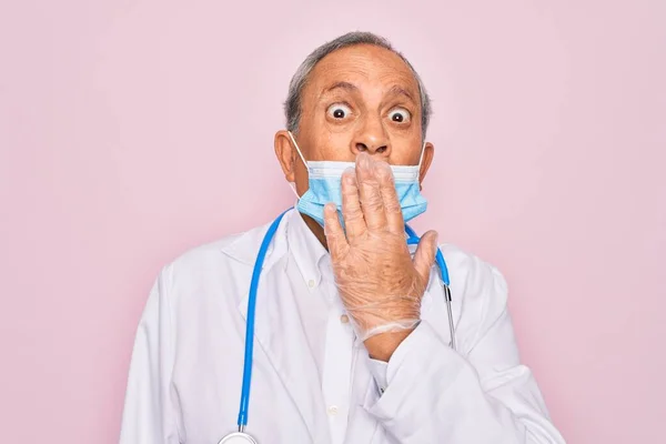 Senior hoary doctor man wearing medical mask and stethoscope over pink background cover mouth with hand shocked with shame for mistake, expression of fear, scared in silence, secret concept