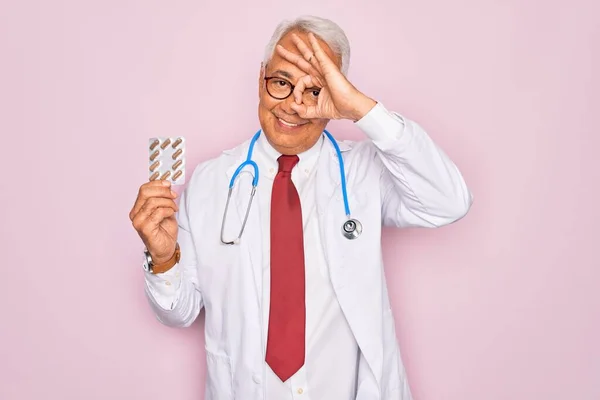中年シニアグレイ髪医師男保持処方薬上のピンクの背景とともに幸せな顔笑顔行いますOk Signとともに手で目を通して指を見て — ストック写真