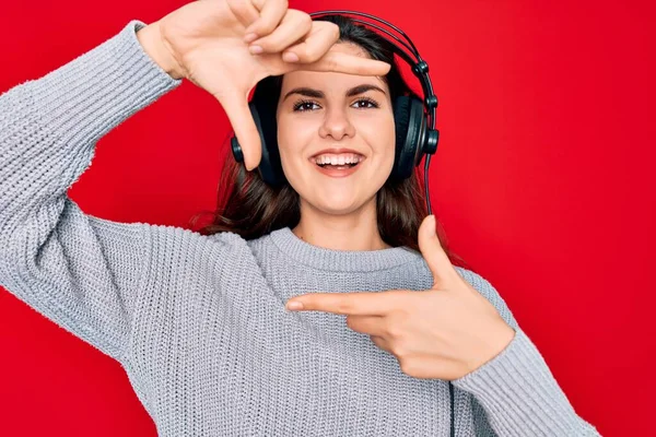現代的なヘッドフォンを身に着けている若い美しい女の子は幸せな顔を持つ手や指でフレームを作り笑いながら赤い背景の音楽に耳を傾けます 創造性と写真の概念 — ストック写真