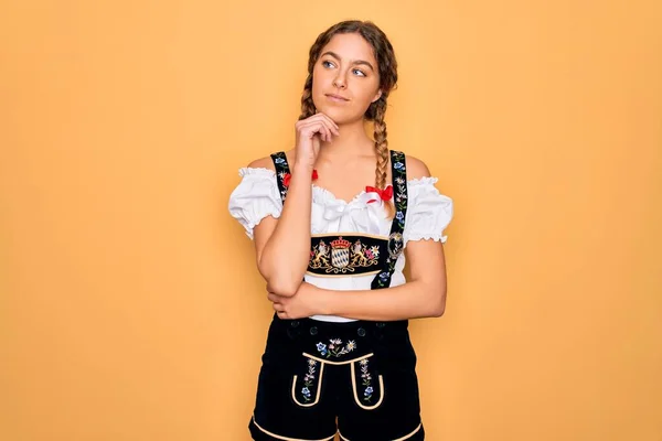 年轻美丽的金发德国女人 蓝眼睛 穿着传统的十月节礼服 手放在下巴上思考着问题 沉思着表情 面带微笑和体贴的脸怀疑的概念 — 图库照片