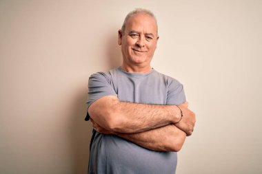 Orta yaşlı, beyaz tişörtlü yakışıklı bir adam izole edilmiş beyaz arka planda duruyor ve kollarını kavuşturup kameraya bakıyor. Pozitif kişi.