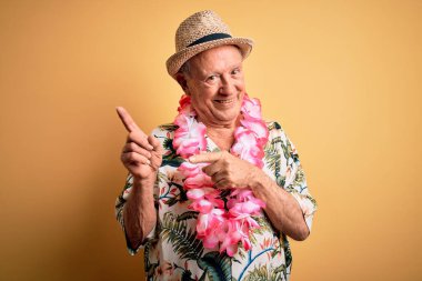 Sarı arka planda beyaz saçlı son sınıf öğrencisi ve Hawaii zambağı takmış mutlu ve komik yüzlü parmakları kameraya doğrultuyor. İyi enerji ve titreşimler.