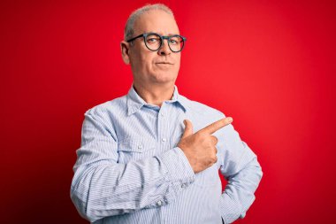 Orta yaşlı, beyaz, sıradan çizgili gömlek ve kırmızı arka planda gözlük takan yakışıklı bir adam. El ile işaret ederek reklamını yapıyor, ciddi ve sakin bir yüz ifadesi var.