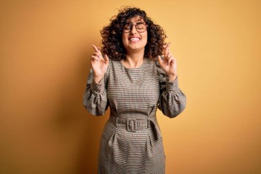 Güzel bir Arap iş kadını. Elbise ve gözlük takıyor. Sarı arka planda duruyor. Şans ve batıl inanç..