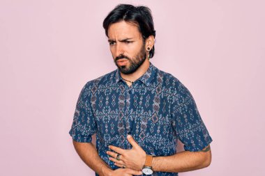 Yakışıklı, İspanyol asıllı bohem bir adam pembe arka planda hippi tarzı giyinmiş midesi üstünde çünkü hazımsızlık, acı verici bir hastalık kendini iyi hissetmiyor. Ache kavramı.