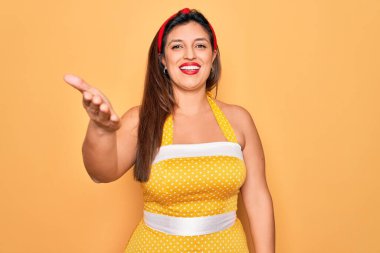 Latin asıllı genç bir kadın, 50 'li yaşlarda seksi giyinmiş sarı arka planda gülümseyerek selamlama ve hoş geldin diyor. Başarılı bir iş..