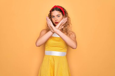 Sarı arka planda duran mavi gözlü güzel sarışın kadın. Reddedilme ifadesi. Kollarını kavuşturma, negatif işaret yapma, kızgın surat.