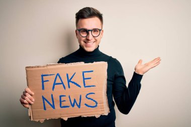 Genç beyaz adam yanlış bilgilendirme ve sahte haberler için protesto kartı tutuyor çok mutlu ve heyecanlı, kazanan ifade zaferi büyük bir gülümsemeyle kutluyor ve ellerini kaldırıyor.